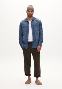 Denimhemd mit zwei Taschen, kombiniert mit einem weißen T-Shirt und braunen hochgerollten Hosen. Abgerundet mit hellbraunen Slippern und einer gestrickten Mütze.