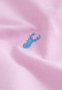 Tela rosa con un tejido texturizado, que presenta un diseño bordado en azul de un ciervo con astas en un lado.