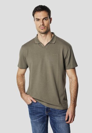 Õlivihreast tekstuurse kangaga v-kaelusega ja lühikeste varrukatega polo, millel on rinnal väike logo. Kandke siniste teksadega.