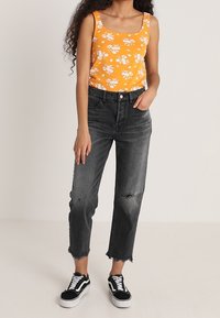 Débardeur floral orange, jeans taille haute gris foncé avec des détails déchirés, et baskets noires avec semelles blanches. Tenue urbaine simple.