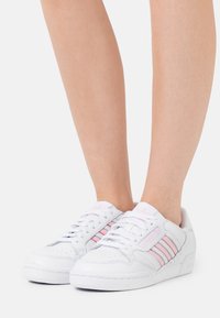 Baltas sneaks ar rozā svītrām, ādas materiāls, noapaļota purngala forma, stieples aizdare, caurumiņu detaļas un neliels papēdis.