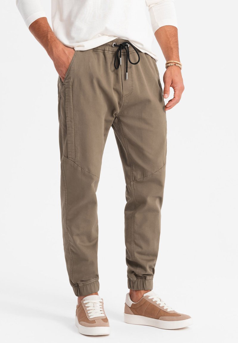 Khaki joggerbroeken met een elastische tailleband en een trekkoord. Gemaakt van katoen, met taps toelopende benen en zijzakken. Gemaakt met lichte sneakers.