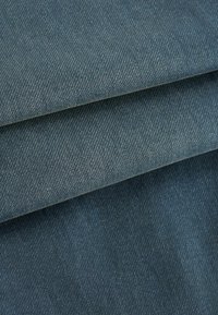 Denim tkanina u tamnoplavoj boji, s karakterističnim twill tkanjem. Tekstura je glatka s blagim sjajem. Vidljivi su preklopljeni slojevi.