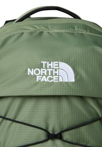 Green nylon backpack featuring a textured grid pattern, black elastic cord detailing, and a white embroidered logo of The North Face.