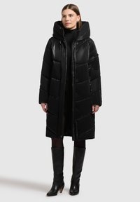 Sort puffjakke med en blank overflade, oversized hætte og knaplukning foran. Har vandrette quiltede paneler og en lang, afslappet pasform.