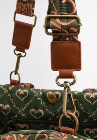 Grüner, gemusterter Taschenriemen mit floralen Designs in Pink, verziert mit braunen Lederakzenten und Messingbeschlägen für sichere Befestigungen.