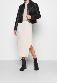 Schwarze Lederjacke mit Kragen, beiger, gerippter Rollkragenpullover, cremefarbener Midirock mit seitlichem Schlitz und schwarze Schnürstiefel.