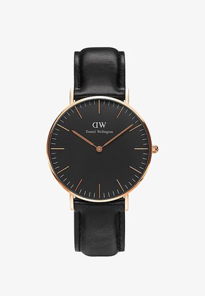 Montre ronde noire au design minimaliste, avec des accents dorés, des aiguilles lumineuses et un bracelet en cuir noir. Présente une disposition simple des marqueurs d'heure.