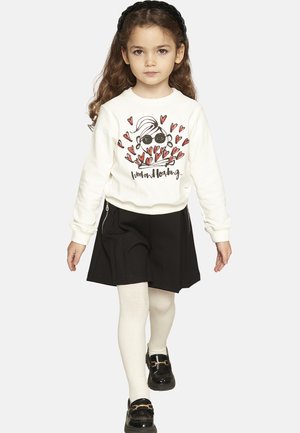 Felpa bianca con grafica di un personaggio e cuori, abbinata a una gonna nera, collant bianchi e scarpe nere con fibbie.