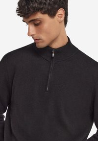 Czarny sweter z zamkiem błyskawicznym przy szyi, wykonany z miękkiej dzianiny. Posiada wysoki kołnierz i półzamknięcie na zamek, z gładkim, teksturowanym wykończeniem.