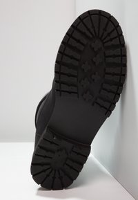 Svart stövelsula med ett texturerat, robust mönster med djupa räfflor och korsformade grepp för förbättrat grepp och hållbarhet.