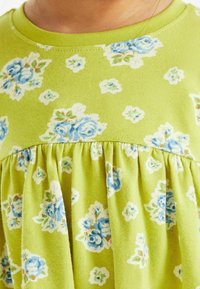 Grön bomullsklänning med blommönster i blå rosor och ljusgröna accenter. Samlad midja och rund halsringning.