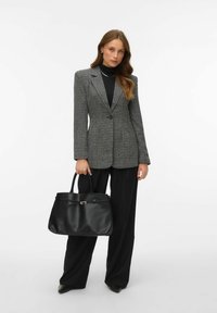 Szary żakiet w wzory z klapami i pojedynczym guzikem, w zestawieniu z czarnym golfem oraz czarnymi spodniami z wysokim stanem. Czarna torba na ramię.