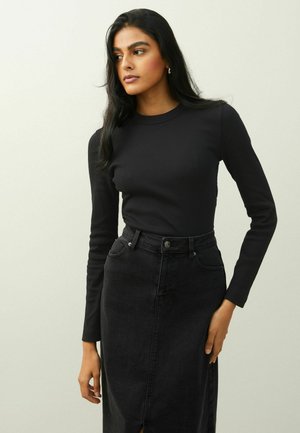 Črna rebrasta majica z dolgimi rokavi v kombinaciji z visokim črnim jeans krilom, ki ima sprednji razrez in klasično gumbno zapiranje.