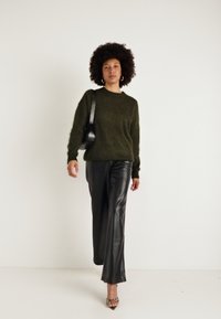 Olive green knitted sweater, czarne spodnie z faux skóry, srebrne sandały na obcasie i mała czarna torebka na ramię. Gładkie tekstury i luźny krój.