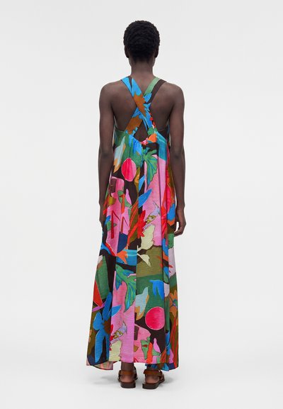 Άτομο που φοράει πολύχρωμο φόρεμα μάξι με floral μοτίβο, σταυρωτούς ιμάντες και ανοιχτή πλάτη, σε συνδυασμό με καφέ σανδάλια.
