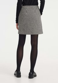 Falda de espiga en blanco y negro con corte recto, que incluye una cinturilla y sin hardware visible, llevada sobre medias negras y zapatos.