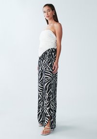 Witte strapless top gecombineerd met loszittende zwarte en witte broek met zebraprint en splitten. Schoeisel bestaat uit witte sandalen met bandjes.