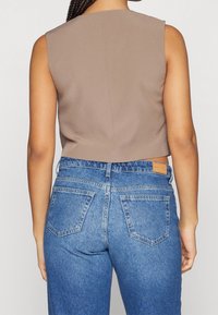 Brun ärmlös topp i cropped stil som matchas med högmidjade blå denimjeans med en urtvättad textur och två bakfickor.