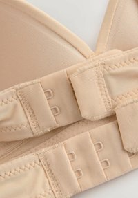 Reggiseno beige con coppe senza cuciture, spalline regolabili e chiusura con gancetti e occhielli con due file di ganci per la regolazione della taglia.