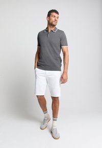 Grijze polo met korte mouwen en witte kraag en mouwt trim, gecombineerd met witte shorts en grijze sneakers, met gestreepte enkelsokken.