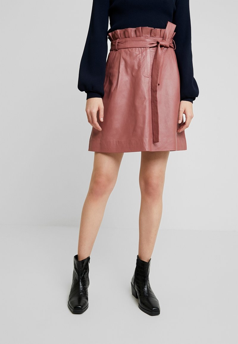 Vaaleanpunainen nahkainen mini-hame, jossa on röyhelövyötärö ja matching-vyö. Sujuva pinta ja levenevä muoto parantavat sen muotoilua.