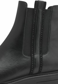 Bottines en cuir noir avec des panneaux latéraux élastiques ornés de pierres noires, bout rond et semelle épaisse pour un peu plus de hauteur.