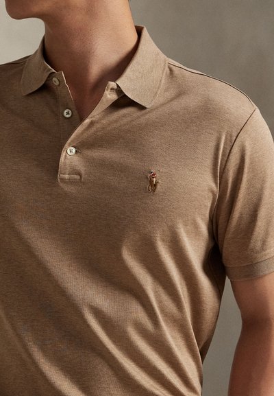 Mann iført lysebrun kortermet polo med lite brodert logo av en polo-spiller til hest på venstre bryst.