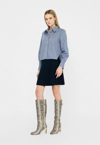 Camicia a quadri blu e bianchi, corta e con bottoni, gonna nera svasata e stivali metallici effetto serpente alti fino al ginocchio con tacco.