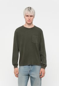 T-shirt à manches longues vert olive en tissu doux, avec un col rond et une poche plaquée sur la poitrine gauche. Coupe décontractée.