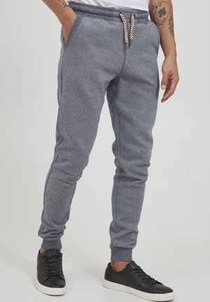 Gray tapered joggers with a textured fabric, elastic waistband, and white drawstring, paired with black sneakers.