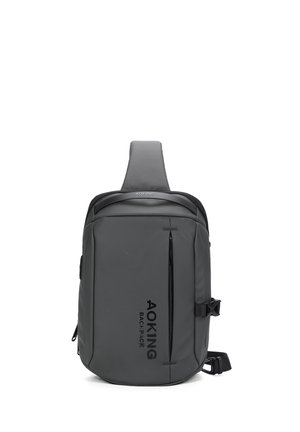 Gray slant backpack made of durable material; features a front zip pocket, adjustable strap, and embossed logo on the side.