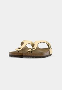 Gelbe Ledersandalen mit geschwungenem Design, verstellbarem Riemen mit Metallverschluss, Korkfußbett und Gummisohle mit strukturiertem Muster.