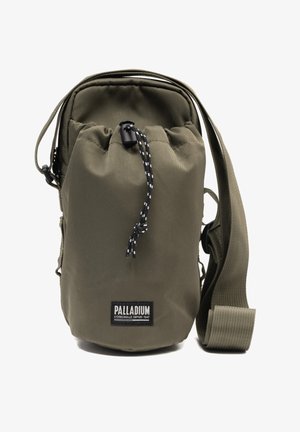 Petit sac bandoulière vert olive avec sangle ajustable, fermeture à cordon et étiquette de la marque Palladium sur le devant.