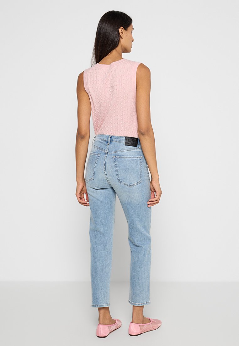 Jasnoróżowy top na ramiączkach z teksturowanym wzorem dzianiny, w zestawieniu z jasnoniebieskimi dżinsami z wysokim stanem i różowymi balerinami, widok z tyłu.