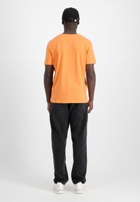 Un tricou din bumbac portocalie cu mâneci scurte, asortat cu pantaloni negri din denim. Tenisi albi și o șapcă neagră completează ținuta. Design simplu.