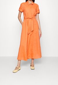 Oranžové lněné šaty s krátkými ohrnutými rukávy, dvěma předními kapsami, páskem v pase a splývavým A-liniovým střihem.