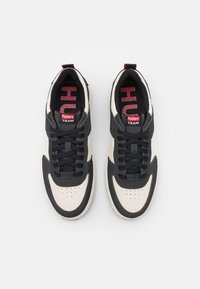 Paire de baskets noires et blanches avec des lacets noirs, une étiquette rouge "Factory Team" sur la languette et un texte rouge à l'intérieur de la semelle, vues de dessus.