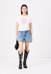 Witte katoenen T-shirt met een roze bloemenprint, gecombineerd met verknipte denim shorts en hoge zwarte cowboylaarzen met zilveren stiksels.