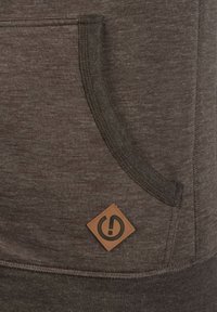 Grijze, weefselachtige stof hoodie met een kangoeroe-pocket, voorzien van een bruine leren logopatch in een diamanten vorm en contrasterende stikdetails.
