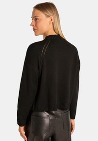 Czarny sweter z dzianiny o skróconym kroju, z prążkowanym dołem i ażurowymi detalami na ramionach. Noszony z czarnymi skórzanymi spodniami.