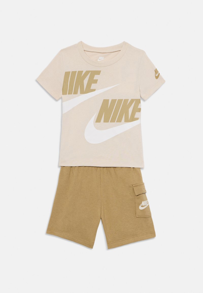 T-shirt di cotone color sabbia con grandi loghi "NIKE" beige e bianchi, abbinata a pantaloni corti sabbia con tasca laterale e dettaglio del logo.