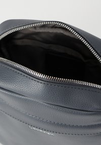 Γκρι δερμάτινη τσάντα χειρός με υφή, που διαθέτει ασημένιο φερμουάρ και ύφασμα επένδυσης στο εσωτερικό. Το εσωτερικό δείχνει βάθος και διαχωρισμό σε διαμερίσματα.