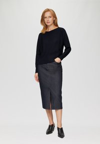 Black knitted sweater with a relaxed fit and ribbed details, paired with a dark denim pencil skirt featuring a front slit. Black heeled mules complete the look.