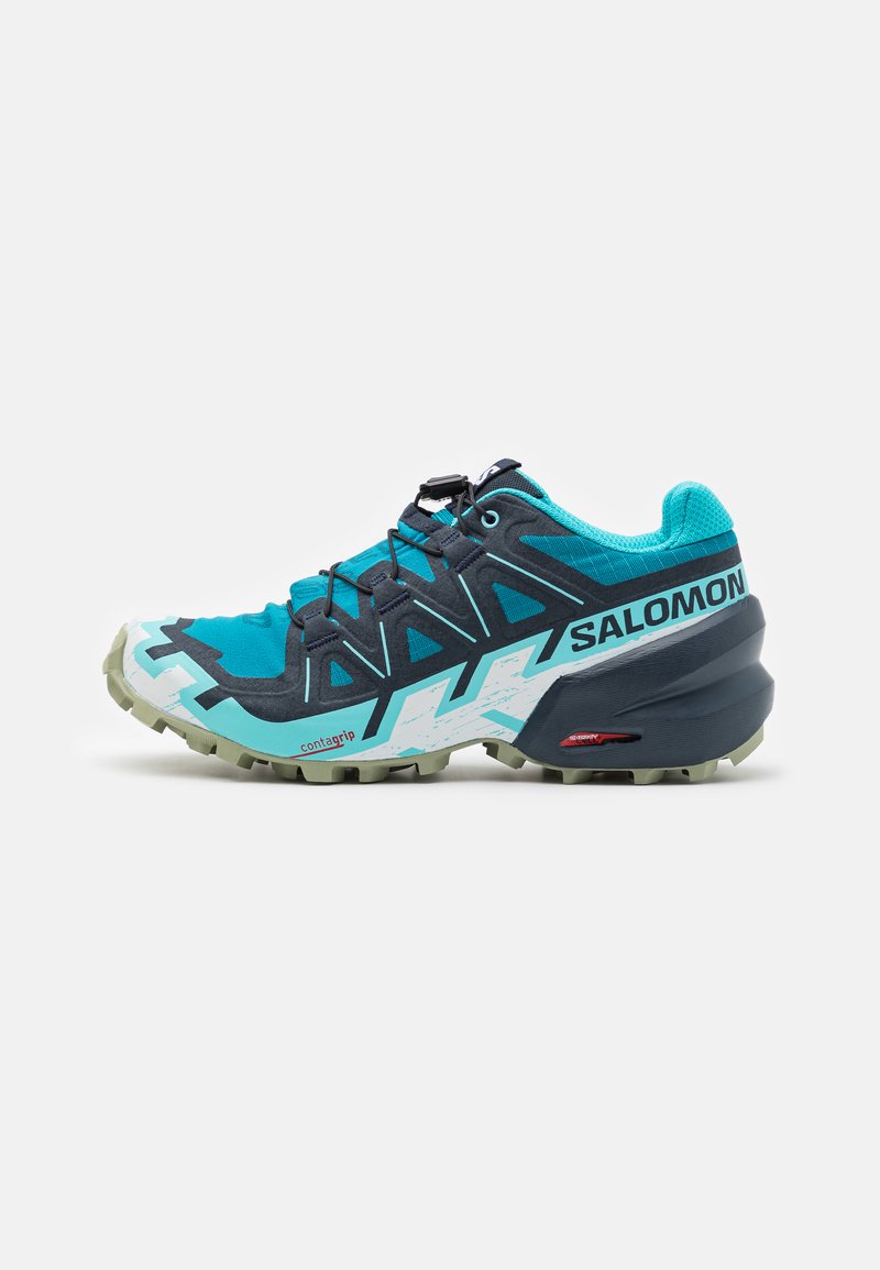 Shoe de trail running em turquesa e navy com um upper texturizado, reforçado com realces escuros, apresentando uma sola contagrip e um sistema de atilhos seguro.