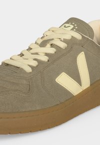 Αθλητικό παπούτσι από ταούπ σουέντ με κρεμ κορδόνια, κρεμ λογότυπο "V" στο πλάι, σόλα από καουτσούκ χρώματος τσίχλας και ετικέτα με αστέρια και "VEJA" στη γλώσσα.