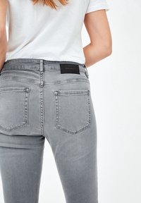 Jeans de mezclilla gris con cinco bolsillos, corte ajustado y una etiqueta negra en la cintura. Textura suave y un patrón de desvanecimiento sutil.