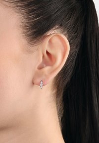 Pendientes de plata con una disposición vertical de tres piedras preciosas redondas y transparentes. Textura suave y diseño moderno, con un acabado pulido.