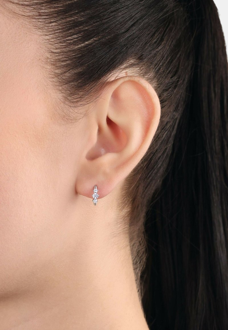 Pendientes de plata con una disposición vertical de tres piedras preciosas redondas y transparentes. Textura suave y diseño moderno, con un acabado pulido.