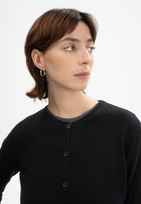 Zwarte cardigan van zachte brei stof, met een ronde halslijn, geribbelde randen en vijf bijpassende knopen aan de voorkant.